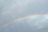 A faint rainbow against a cloudy sky