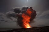 A red fire with smoke billowing from it burns against a grey sky.