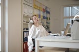 woman with headphones on snoozes in front of her desk.