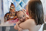 mother holding baby while painting a picture