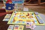 Spielaufbau des Schmidt Spieles “Paddington Bär geht einkaufen”. Zu sehen ist ein typisches Spielbrett mit aufgedeckten Karten, sowie offen liegenden Punkten. Figuren sind auf das Spielbrett platziert, um einen Testaufbau zu symbolisieren.