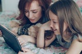 Image of a woman and a younger girl smiling and looking at a tablet