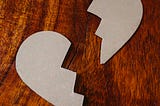 A cardboard heart shaped object broken in two on a wooden table
