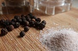 close-up of black peppercorns next to pink himalayan salt on bamboo cutting board