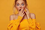 young woman with clothes full body shot, being surprised, open mouth, one hand covering the mouth. Indoor studio shot, contrasting, single vivid color background color codes