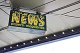 Neon sign at news agent mentioning news, papers, and magazines.