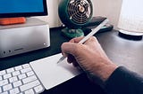 A hand holding an Apple Pencil over a Magic Trackpad