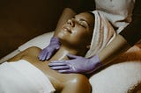 Picture of a black woman in a towel receiving a massage from a gloved professional