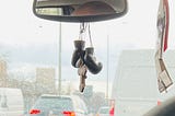 A big wooden cross and a pair of mini boxing gloves hanging from a rearview mirror