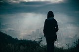 Silouette of woman standing on a hill looking at bleak landscape.