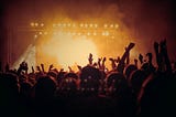 image of a concert with stage lights in background and crowd with hands lifted in silloutette foreground.