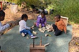 children sitting in an outdoor classroom playing with blocks.