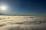 A muted, fuzzy photo above the clouds, with the bright sun in the corner, possibly from an airplane window.