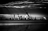 Silhouette of a power plant with cooling towers and trails of clouds.