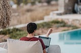 A digital nomad sits behind his laptop overlooking a swimming pool