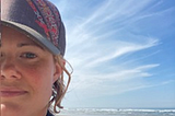 A person who is wearing a purple hat stands by the beach.