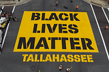 An overhead view of an intersection in Tallahassee. A yellow square is filled with black text stating “Black Lives Matter” Tallahassee.