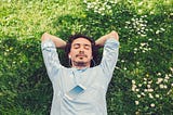 Relaxed man lying down at the meadow and listening to music