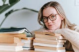 Woman wearing glasses with stacks of books