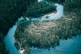 A beautiful aerial photo of a vivid blue river bordered by thick, green forests.