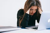 Woman rubs temples while staring at laptop