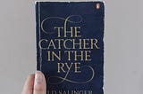 Fariza’s hand holding The Catcher in the Rye book in front of a cream colored background