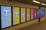 A line of ad displays with each screen a different color and the MBTA logo