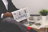 Bottom half of man on chair with business newspaper