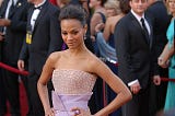 Actress Zoe Saldana in a sleeveless shimmering pink and lavender gown in front of a red rope.