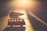 Picture depicts a toy van with a tiny Christmas tree strapped to the roof.