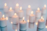 the photograph shows 12 lit white candles against a white backdrop