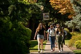 Three college students wearing masks and walking on a paved path.
