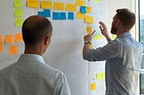 Two men working on a whiteboard full of Post-it notes