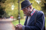 An older man sits outside while using his phone.