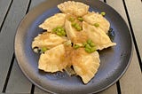 A plate of delicious pierogie ruskie, topped with fried onion and edamame beans