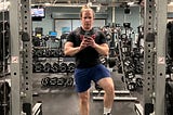 The author, taking a mirror selfie near a powerlifting rack.
