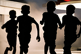 Silhouettes of four boys running away from a gas station at night.