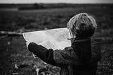 Child looking at map facing an open field.
