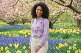 A woman in pastel ruffle blouse and light-wash trousers against a beautiful spring scene