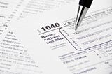 A US 1040 tax form being filled out with a pen