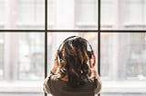 woman looking out a window with headphones on, listening to binaural beats.