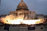 A photo of smoke in front of the U.S. Capitol Building; Trump 2020 flags can be seen hanging in front of a crowd of rioters.
