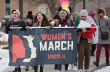 Picture of (left to right) Mar Lee, Guadalupe Esquivel, and Arlenne Rodriguez holding the 2019 Lincoln Women’s March banner.