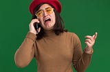 Young woman crying while on the phone, wearing a red hat. The background is green.