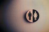 A restroom sign that is half white and black with male on one side and female on the other side, similar to a yin and yang symbol.