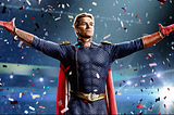 Blonde, white man in a red, white, and blue superhero costume with his arms outstretched, standing on a stage while confetti falls in the background.