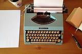 An antique typewriter with a blank sheet of paper on a wooden desk.
