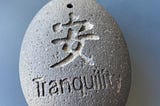 oval stone with the word “Tranquility” and a Chinese character engraved on it.