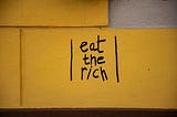 “eat the rich” written on a yellow wall