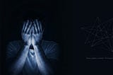 A man sitting in total darkness, covering his face with his hands, illuminated by a deep blue light.